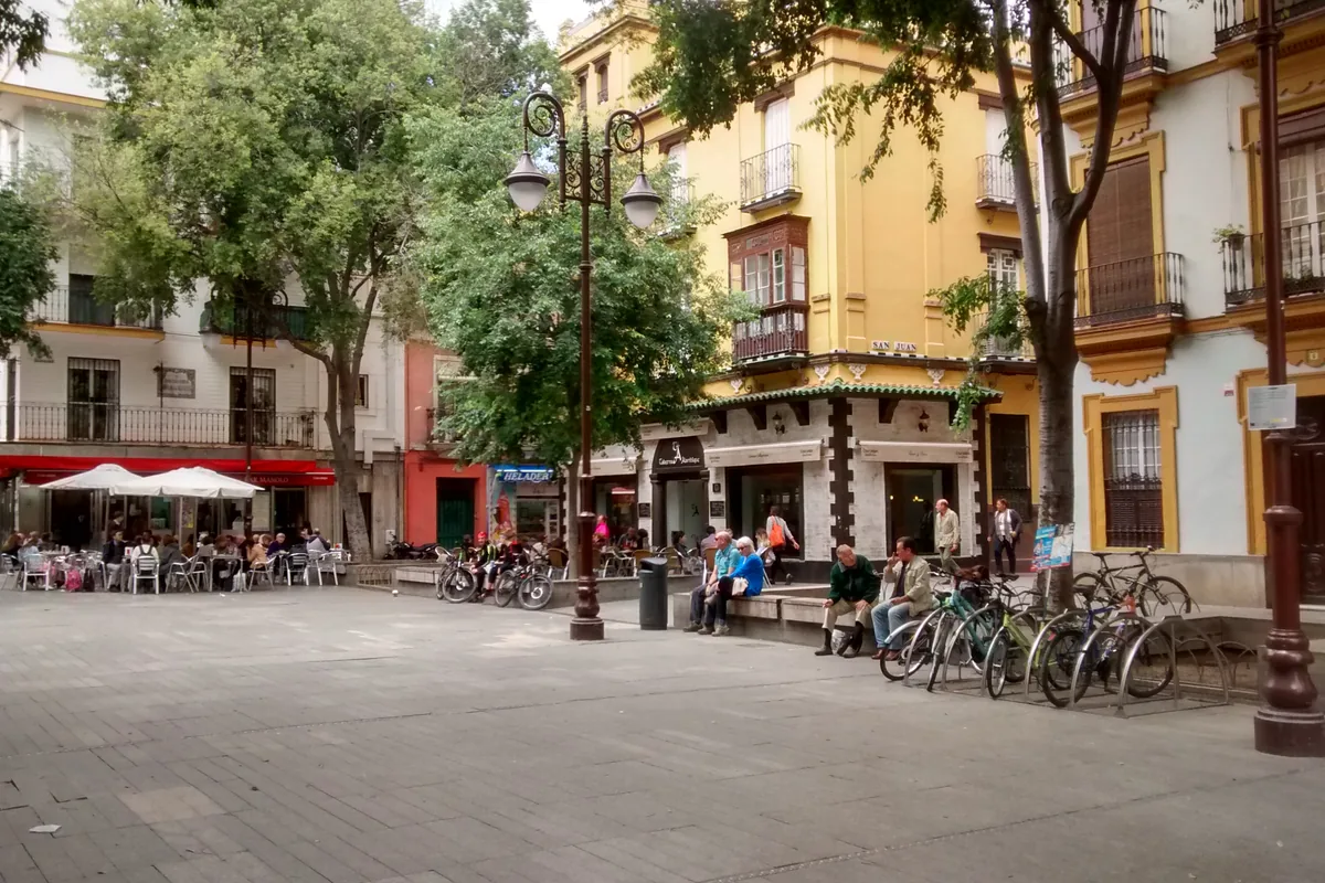Plaza de la Alfalfa a Siviglia: una piazza pavimentata con tavolini da caffè sotto gli alberi, biciclette nei rastrellieri ed edifici gialli e bianchi con balconi